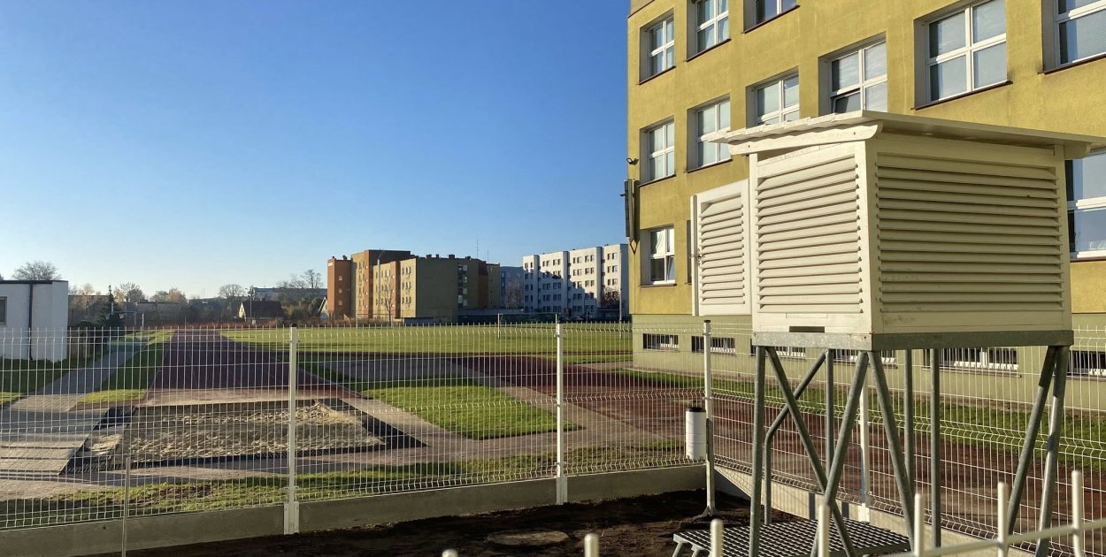 Szkolna stacja meteo z klatką meteorologiczną i deszczomierzem.